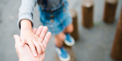 Young child balancing on wooden poles holding onto to outstretched hand from grown up